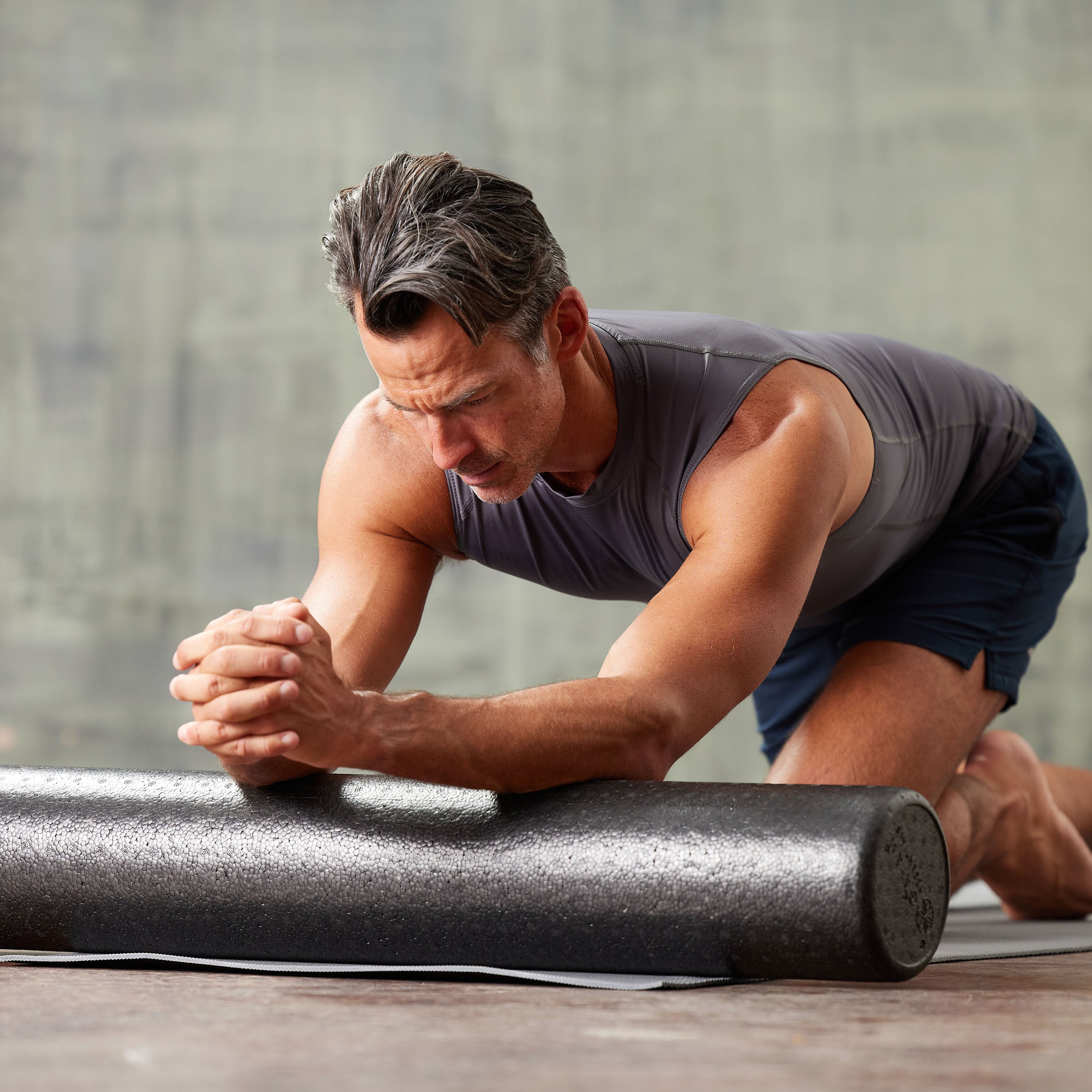 Person using the Essentials High-Density Foam Roller to massage the arms while kneeling on the ground