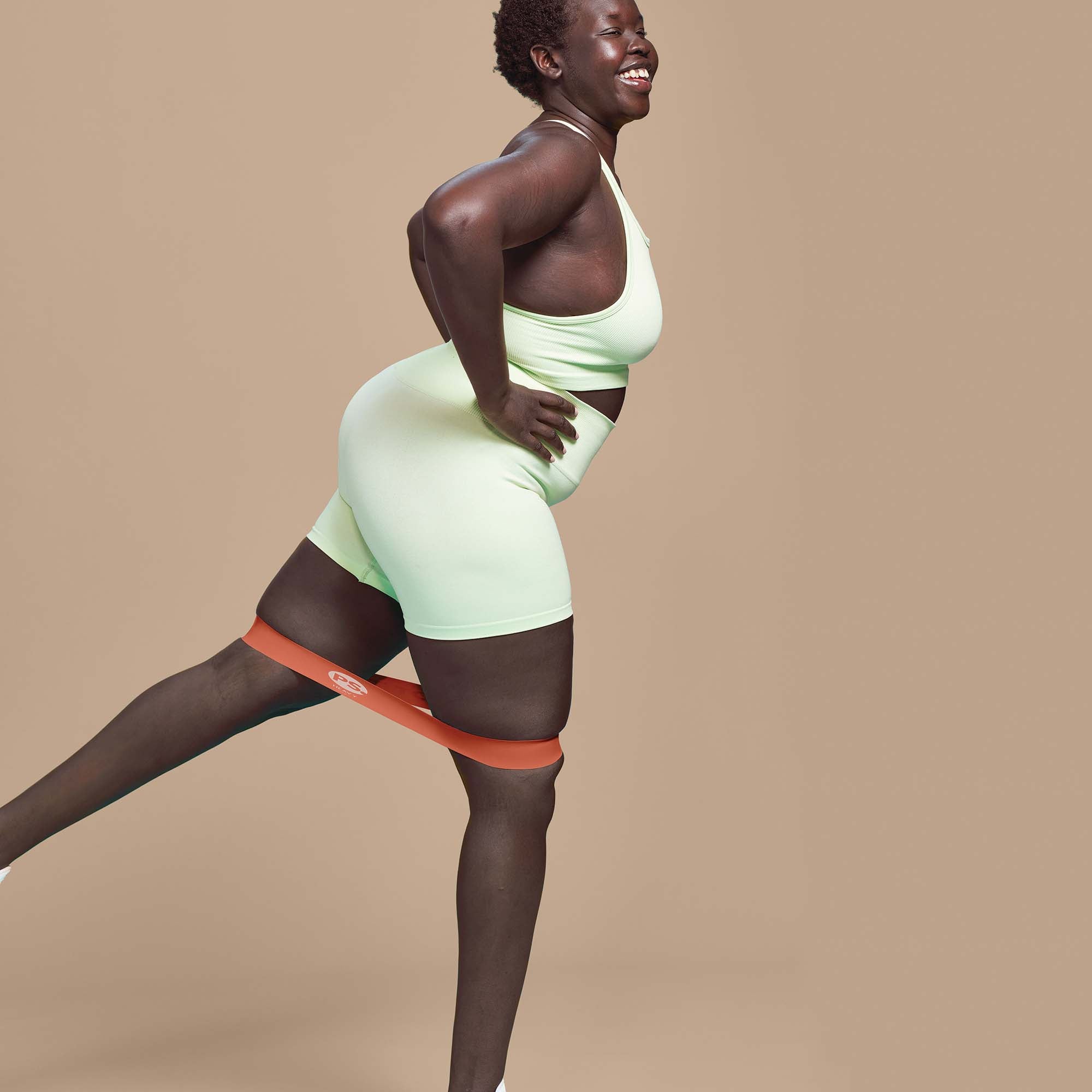 Person wearing a POPSUGAR mini band around the upper legs while standing and doing a glute leg lift